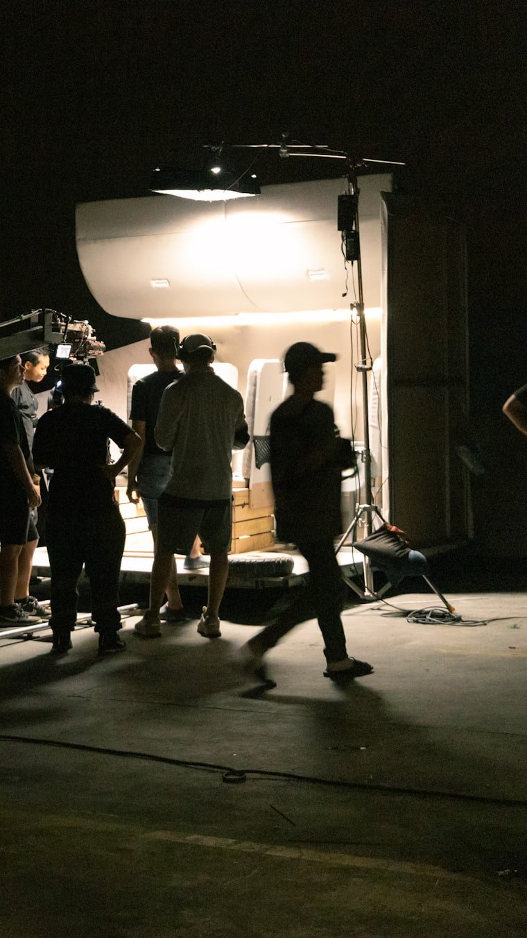 A film crew silhouetted against a lit set at night.
