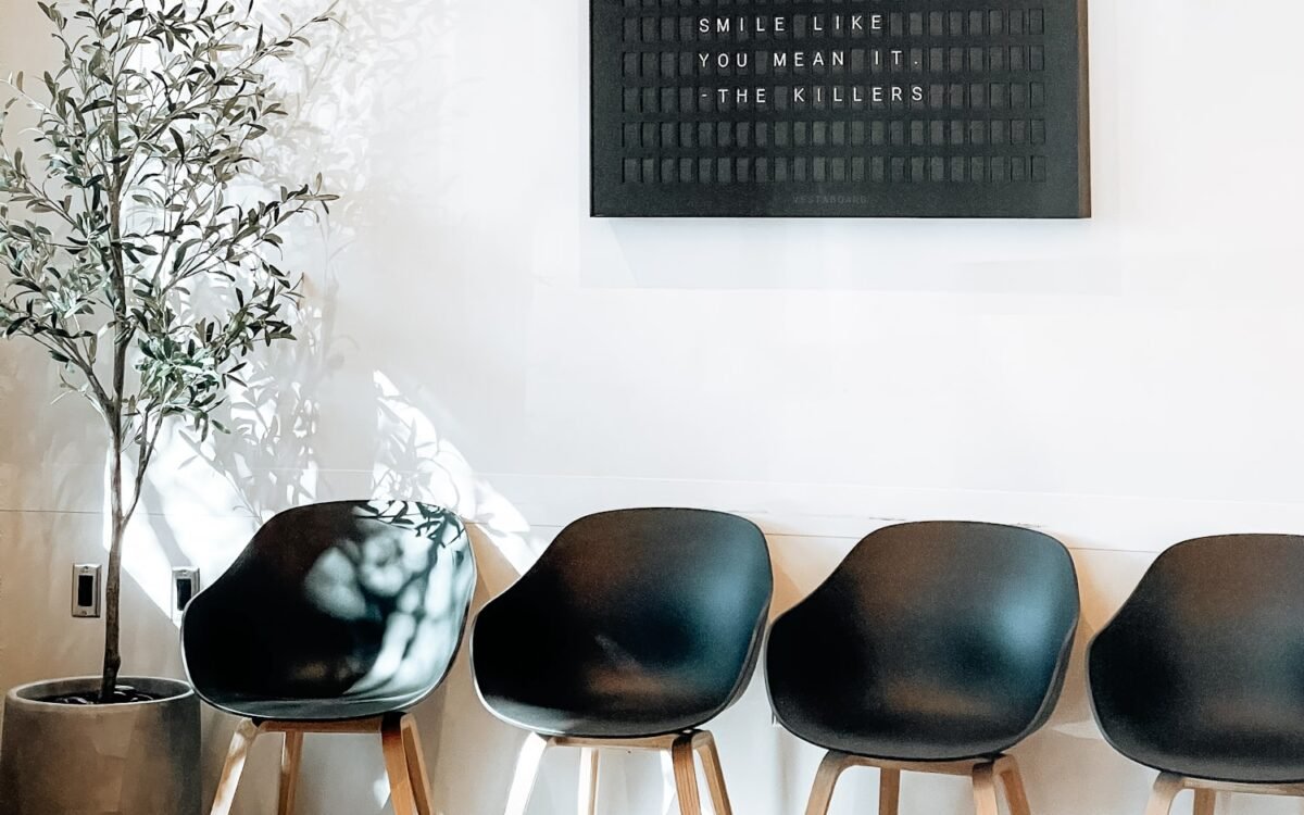 A calm modern clinic waiting room with dark chairs and an olive tree.